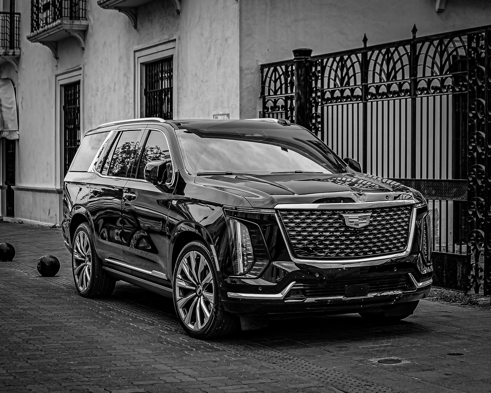 Black SUV parked beside an ornate iron gate, black and white